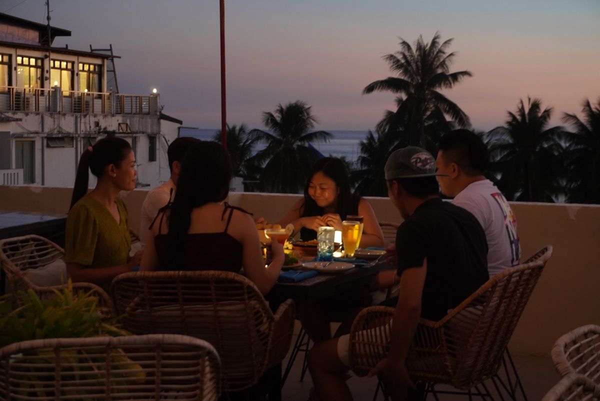 Guests dining on the rooftop as the sky turns pink behind the palms.