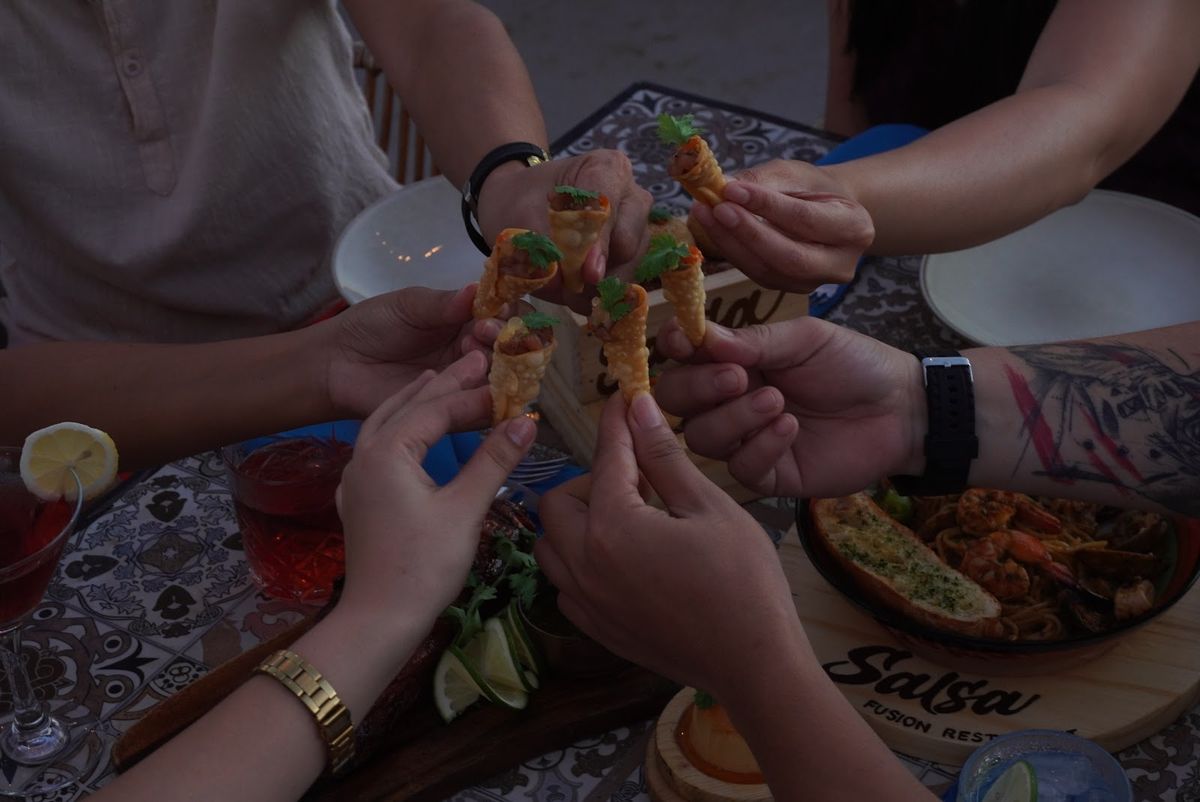 Friends clinking tacos together over the table.